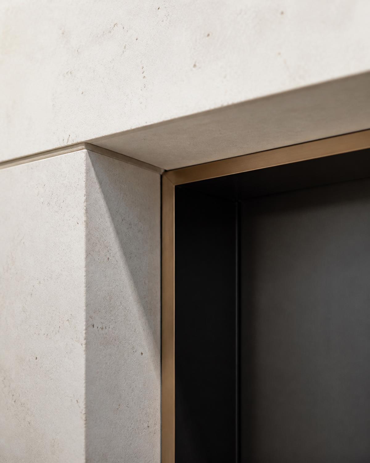 Detalhe construtivo: encontro entre pedra clara, metal escuro e perfil discreto em bronze