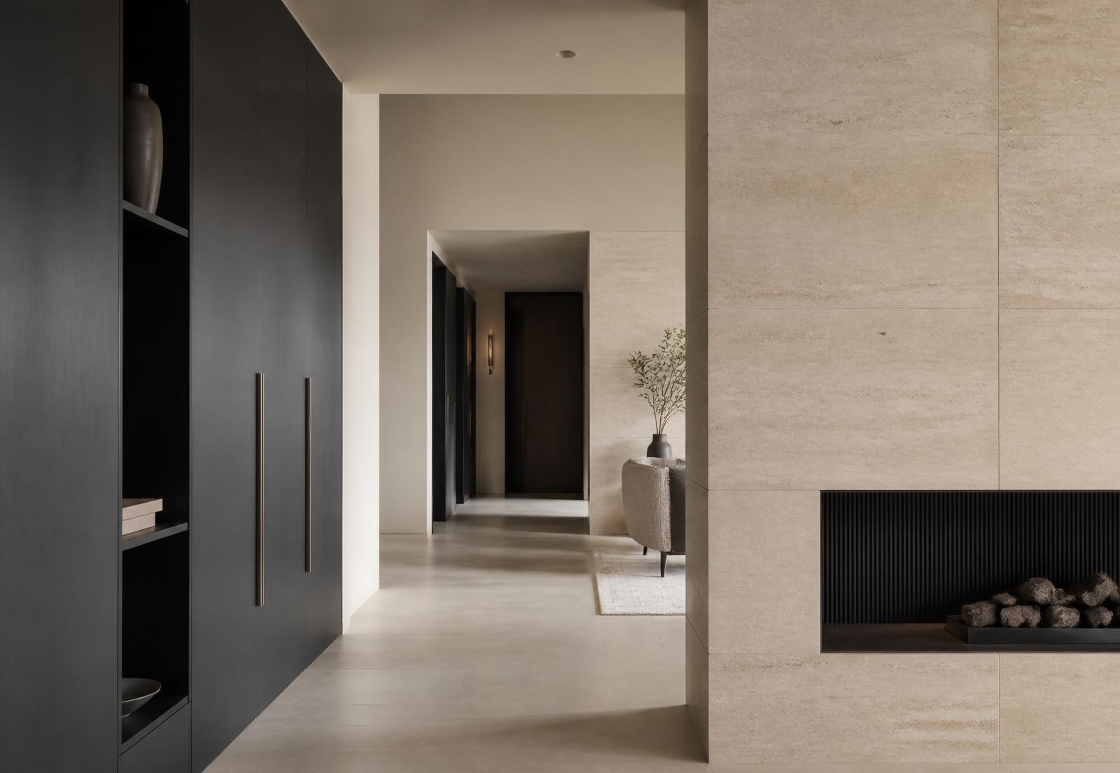 Interior de alto padrão com parede em travertino, marcenaria em grafite e detalhe em bronze